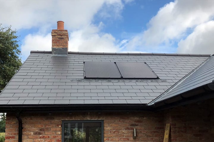 Solar Panels on a black roof with a blue sky and clouds behind 