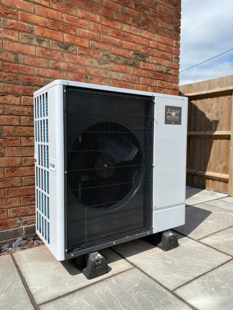 A Mitsubishi Air Source Heat Pump infront of a brick wall