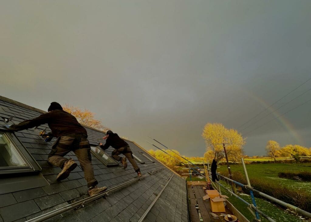 Two green building renewables installers fitting solar panels to a roof with a rainbow in the background