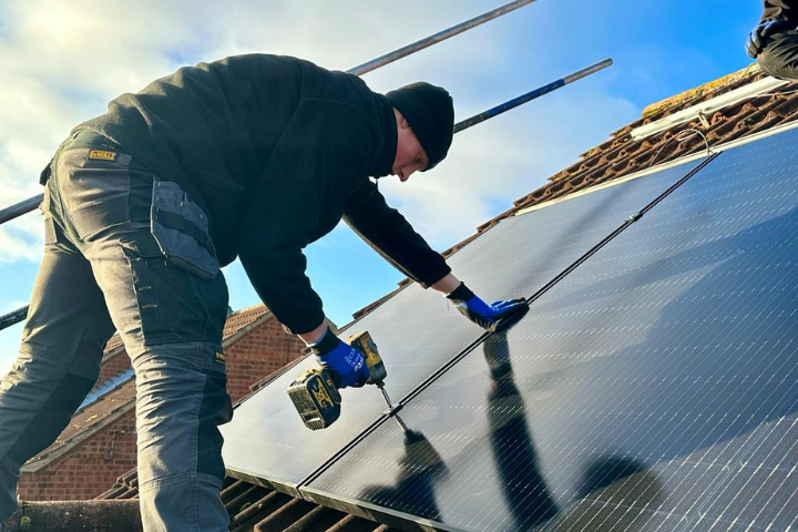 A green building renewables installer fitting solar panels on a roof